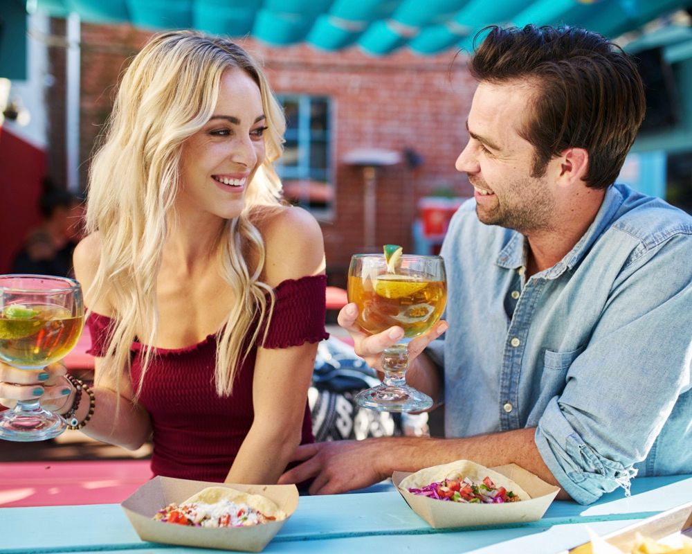 Attractive romantic couple holding beers at mexican restaurant about to eat tacos