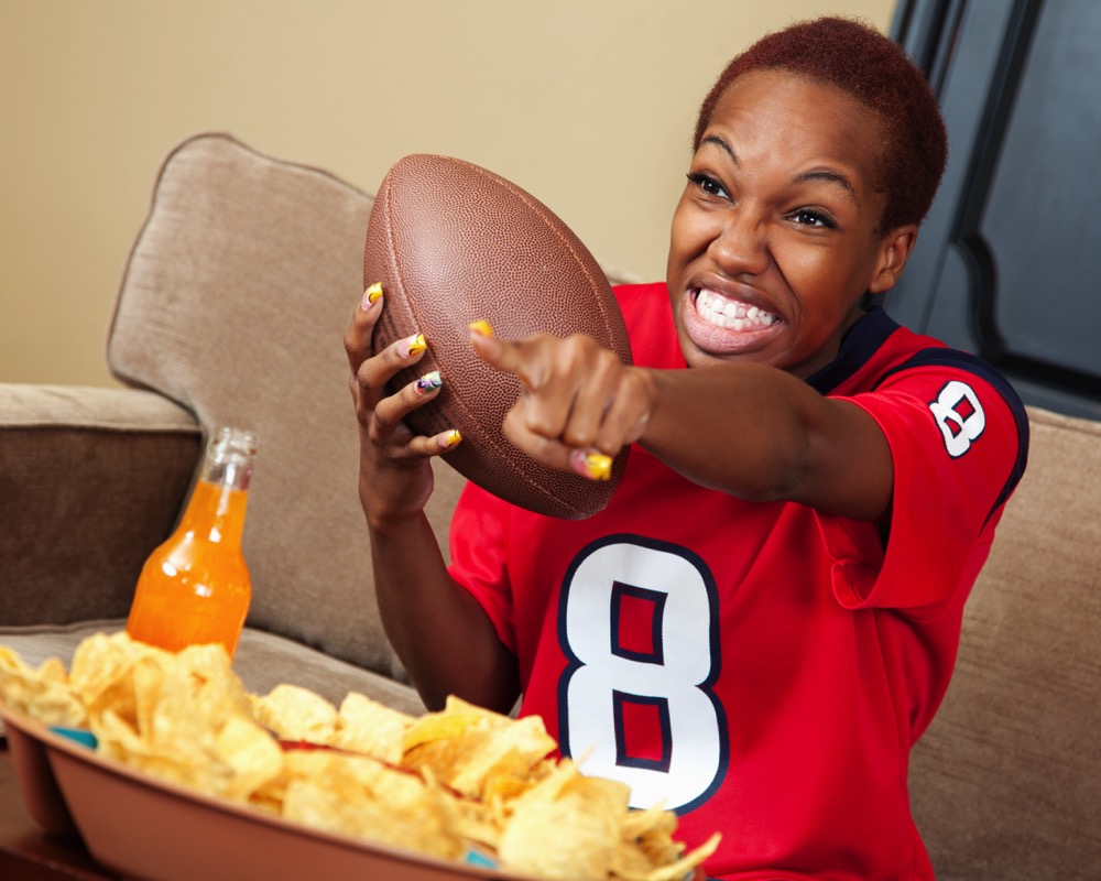 Excited female fan cheering her football team on TV stock photo